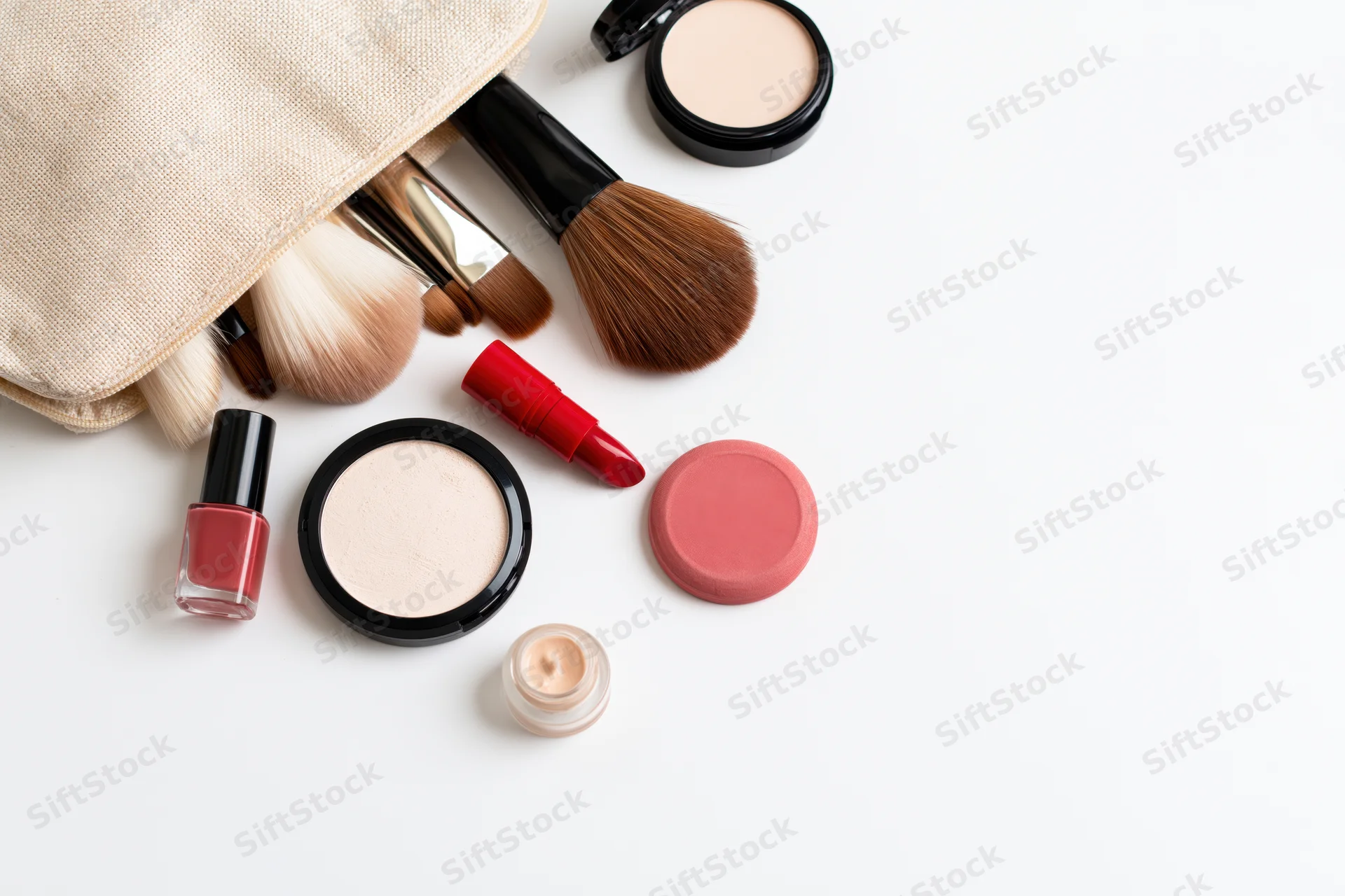 Makeup products spilled from a cosmetic bag arranged on white surface with copyspace