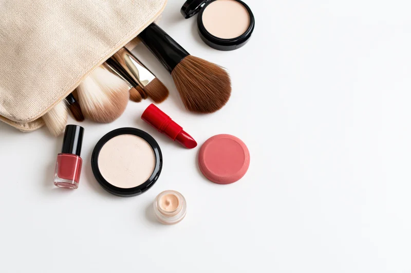 Makeup products spilled from a cosmetic bag arranged on white surface with copyspace