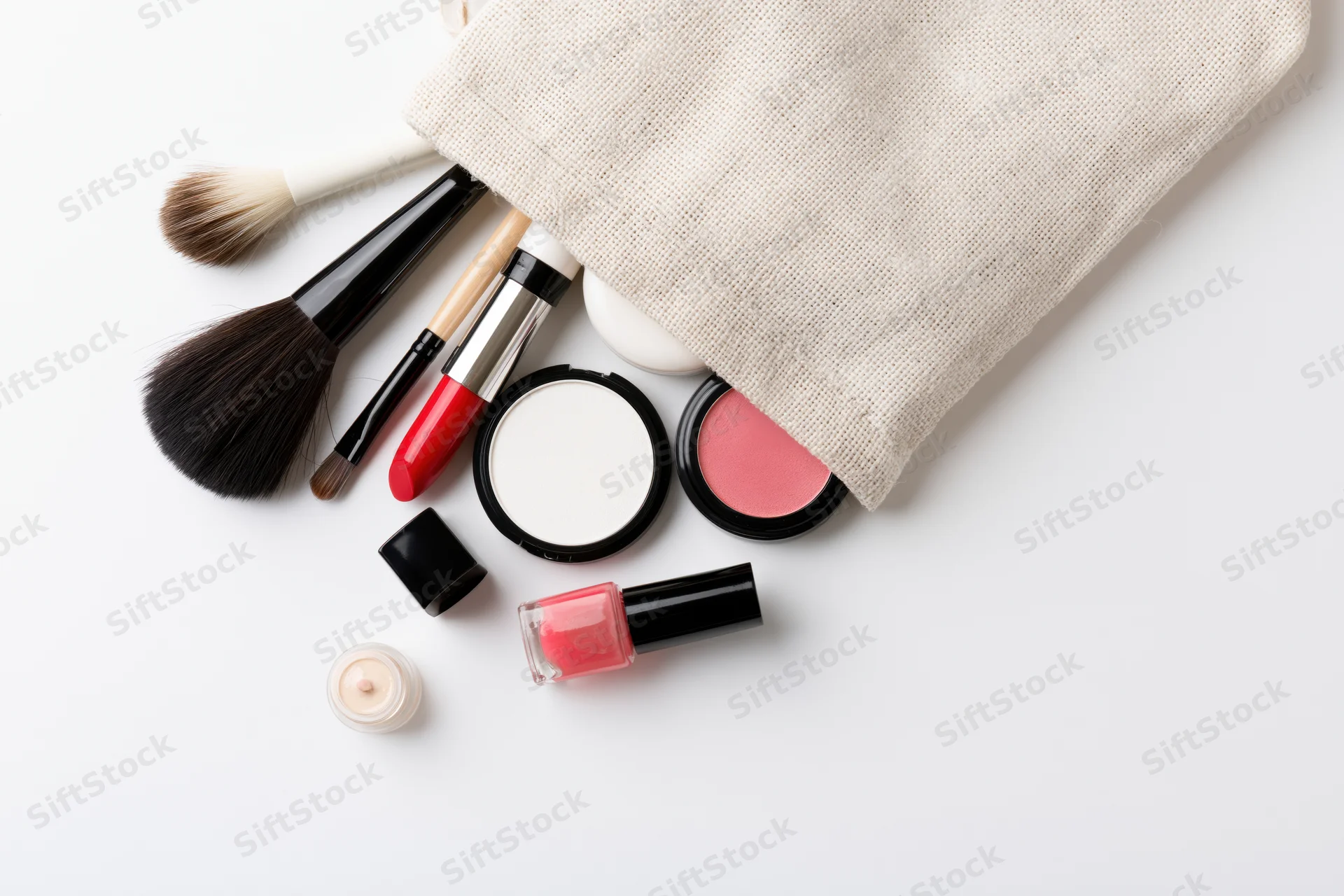 Makeup products spilled from a beige cosmetic bag on white surface
