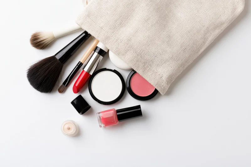 Makeup products spilled from a beige cosmetic bag on white surface