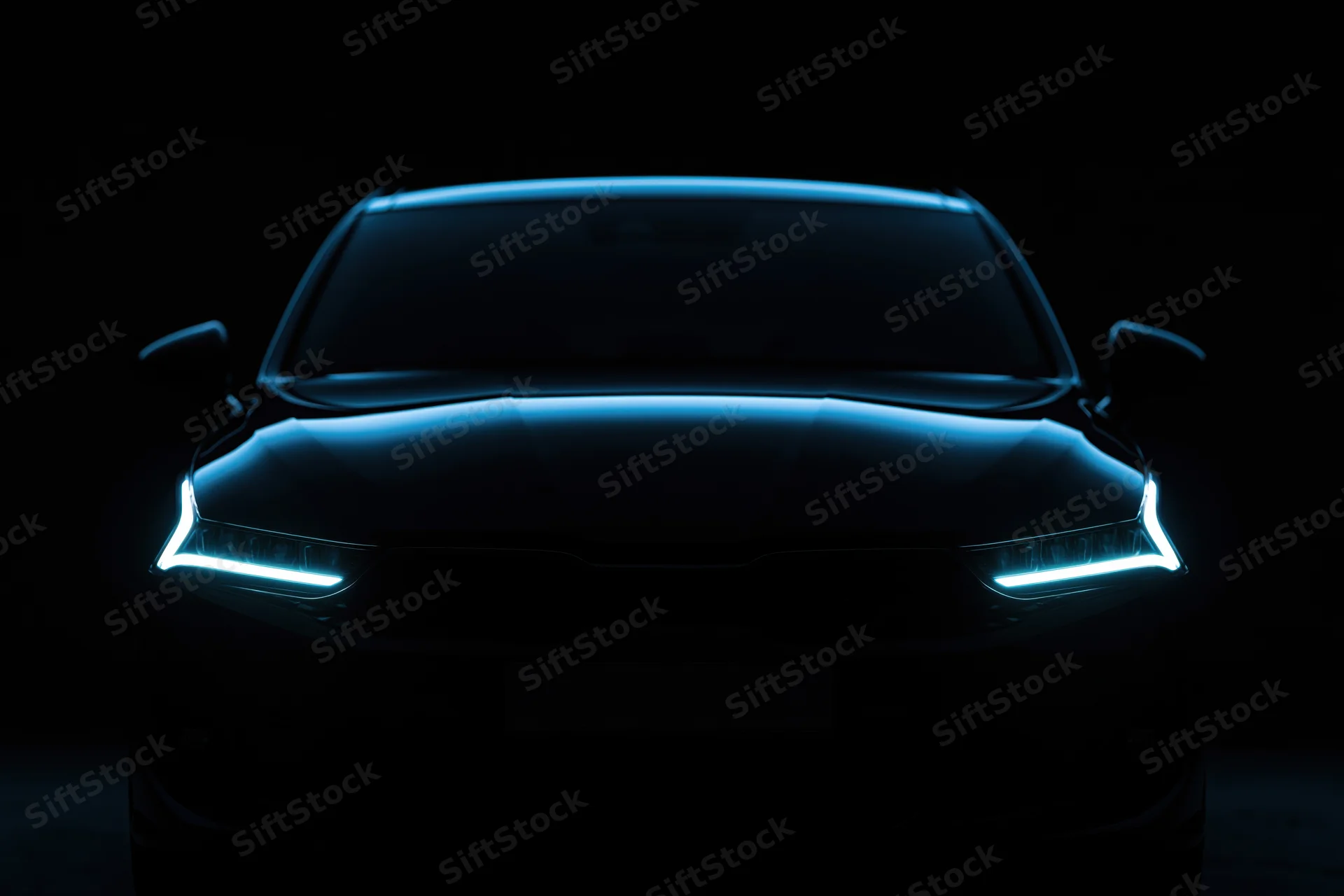 Modern sedan front view with glowing blue headlights in dark studio setting