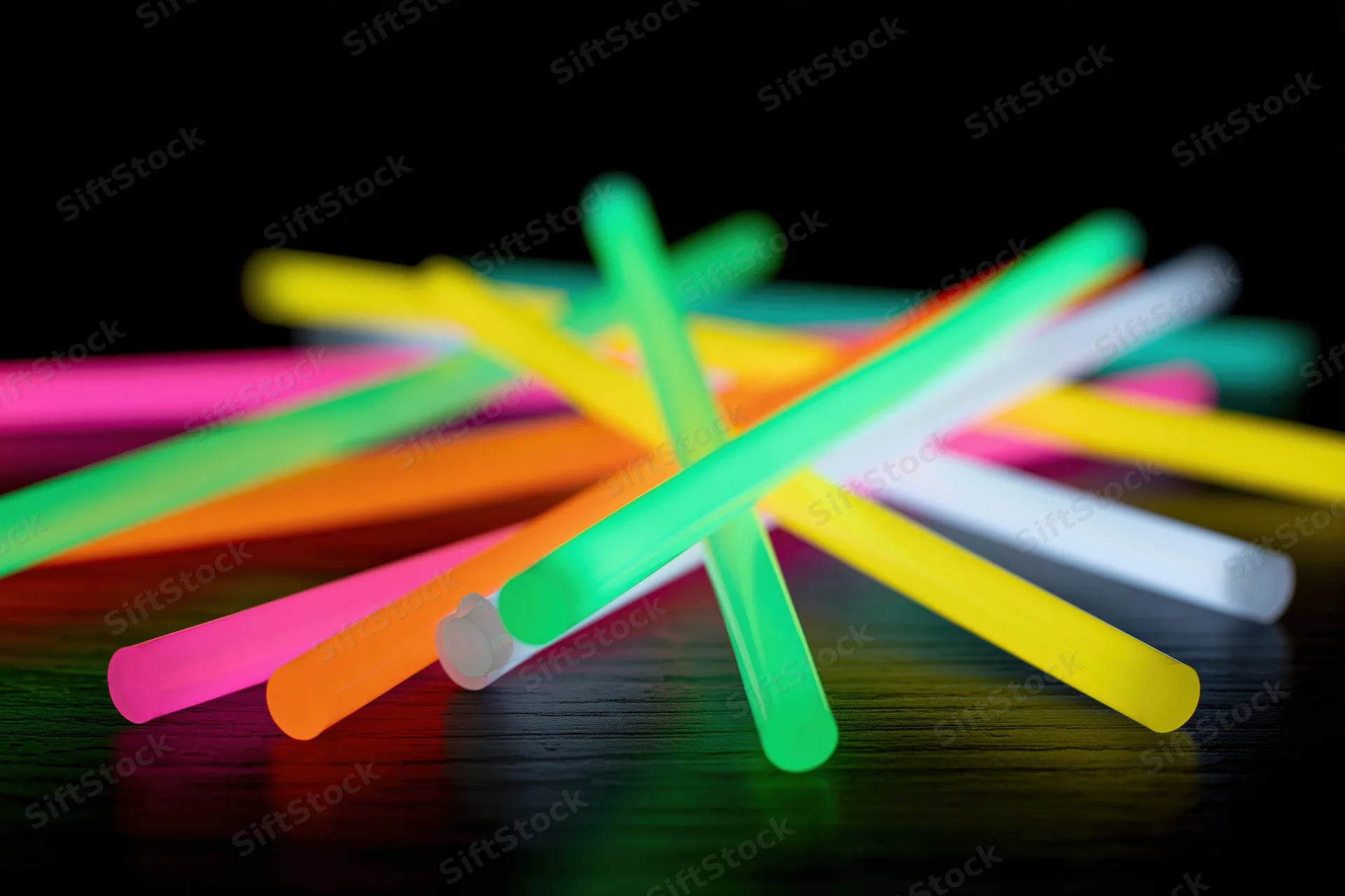 Glowing neon sticks scattered and crossed on a dark wooden surface