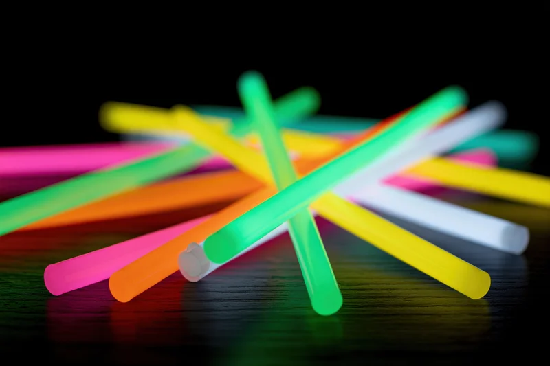 Glowing neon sticks scattered and crossed on a dark wooden surface
