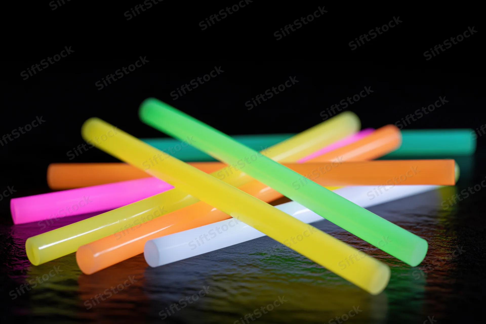 Multiple glowing neon glow sticks scattered and crossed over on a dark reflective surface