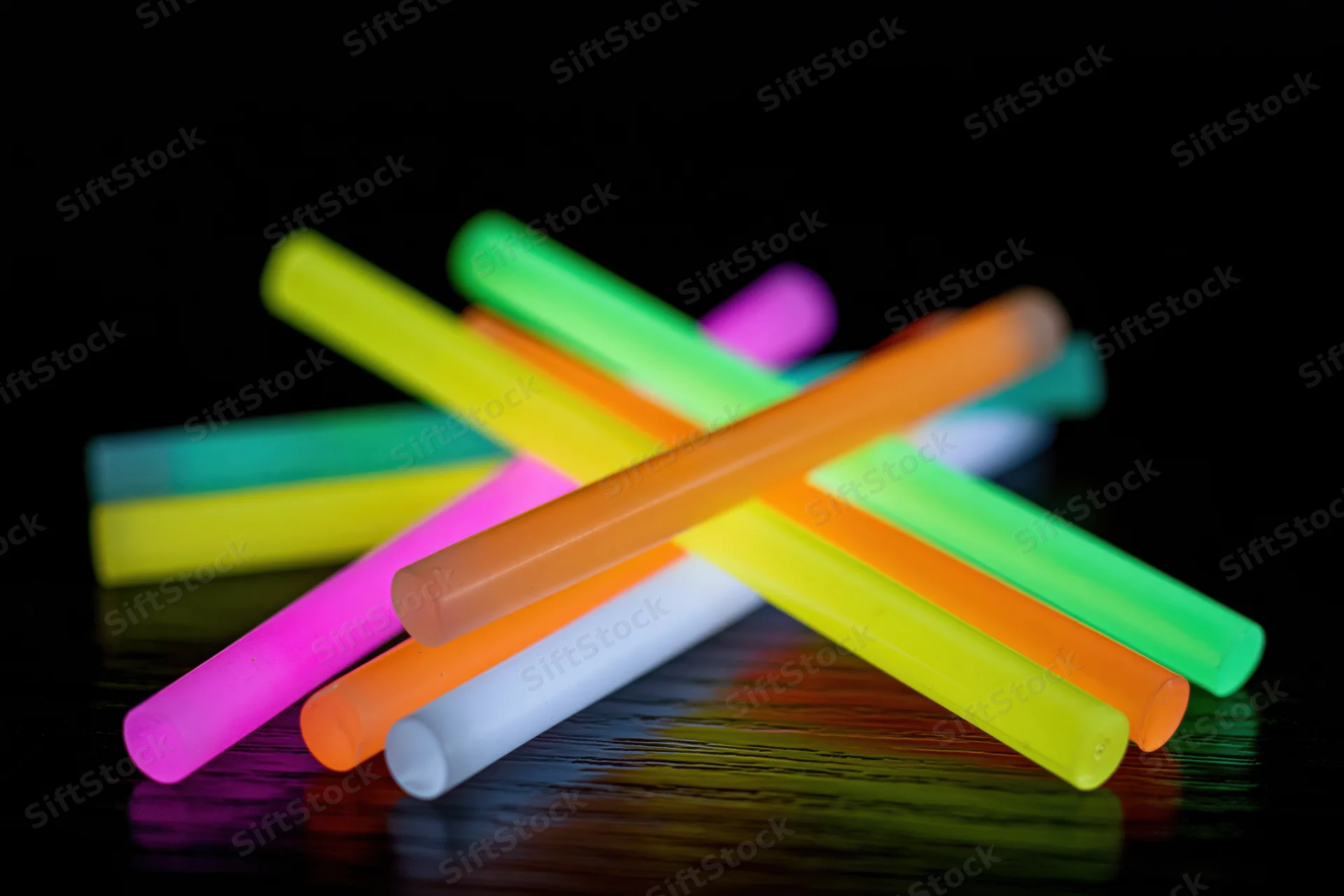 Colorful glow sticks scattered and crossed on a dark reflective surface