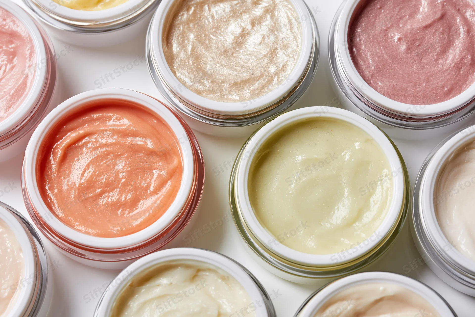 Open cosmetic cream jars arranged in a flat lay grid on white surface