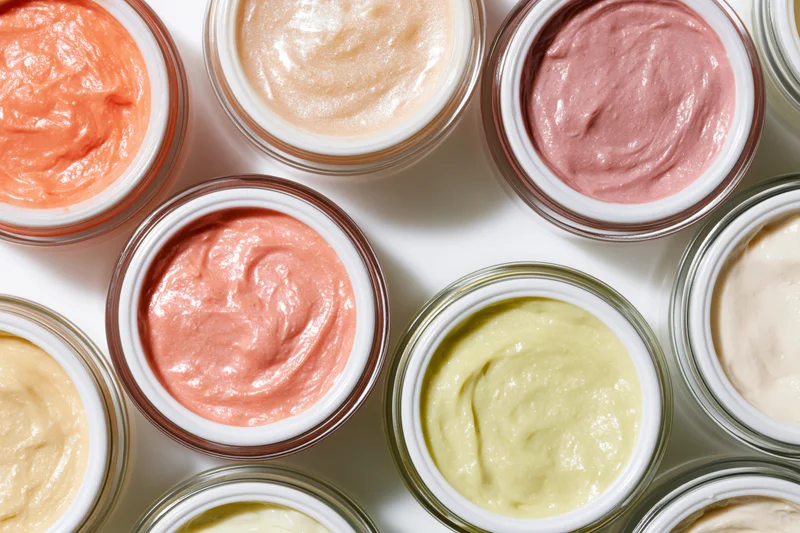 Open cosmetic cream jars arranged in a flat lay grid on white background
