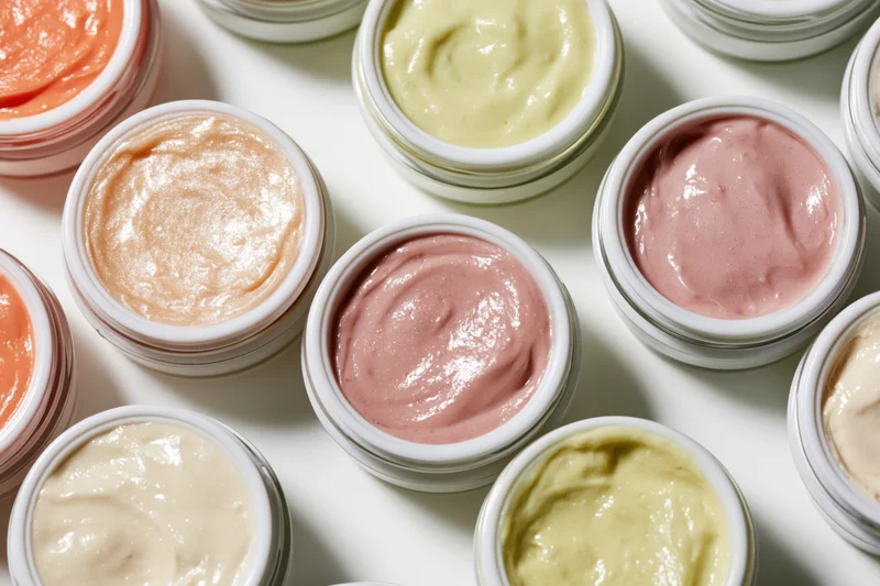 Open cosmetic cream jars arranged in a flat lay grid on white surface