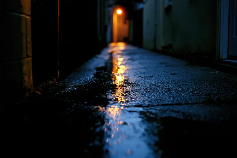 Wet concrete alley at night with glowing light reflection on pavement