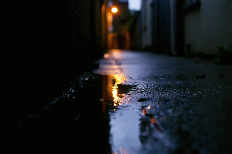 Narrow urban alley at night with wet concrete reflecting streetlight glow