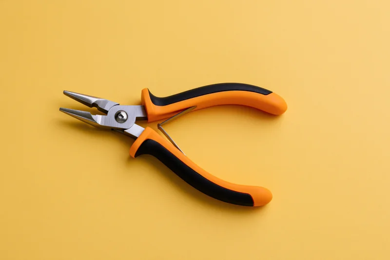 Needle-nose pliers lying open on a flat yellow background