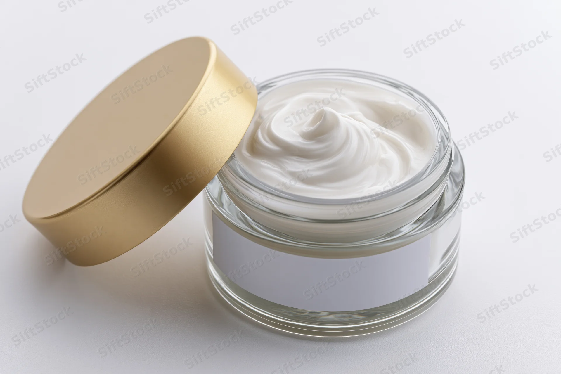 Open glass jar with white swirled cream and gold lid on white surface