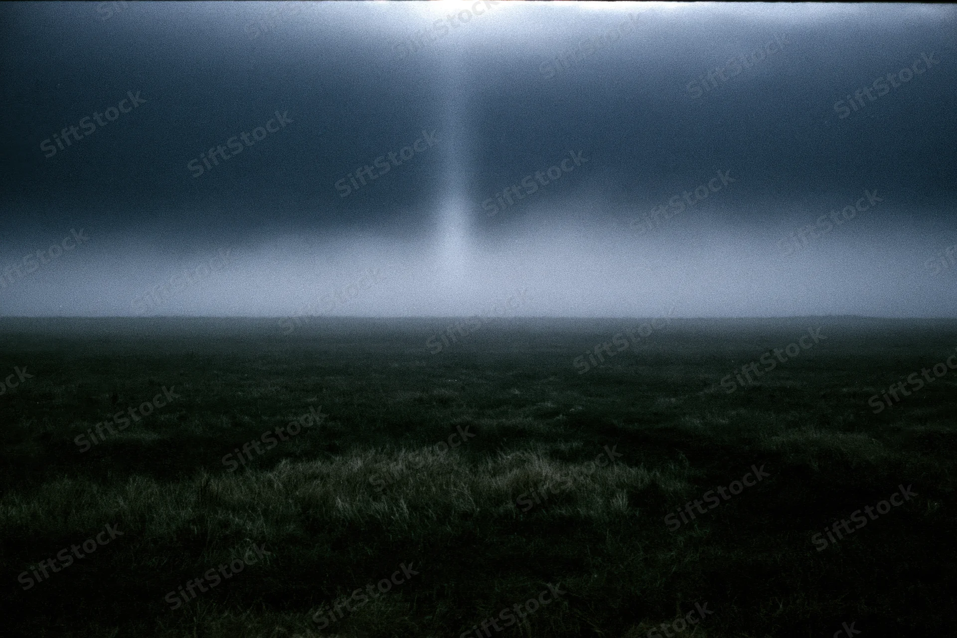 Dark foggy field at night with low ground mist drifting across open grassy terrain