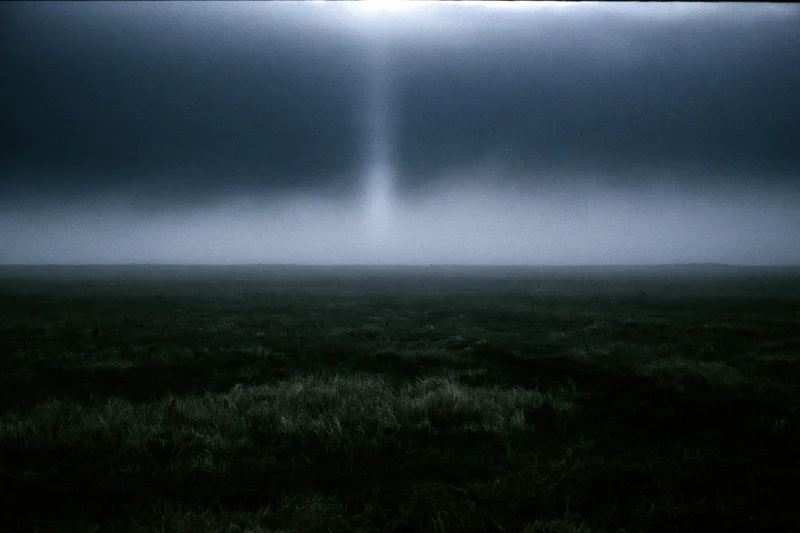 Dark foggy field at night with low ground mist drifting across open grassy terrain