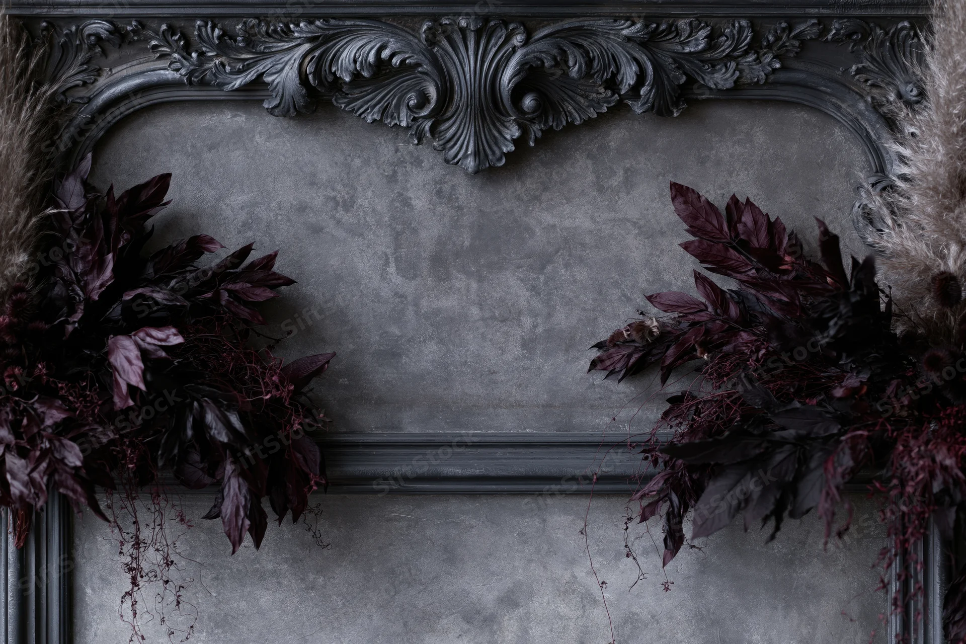 Ornate black baroque frame with dark dried botanicals arranged on a textured plaster wall, featuring copyspace in the center