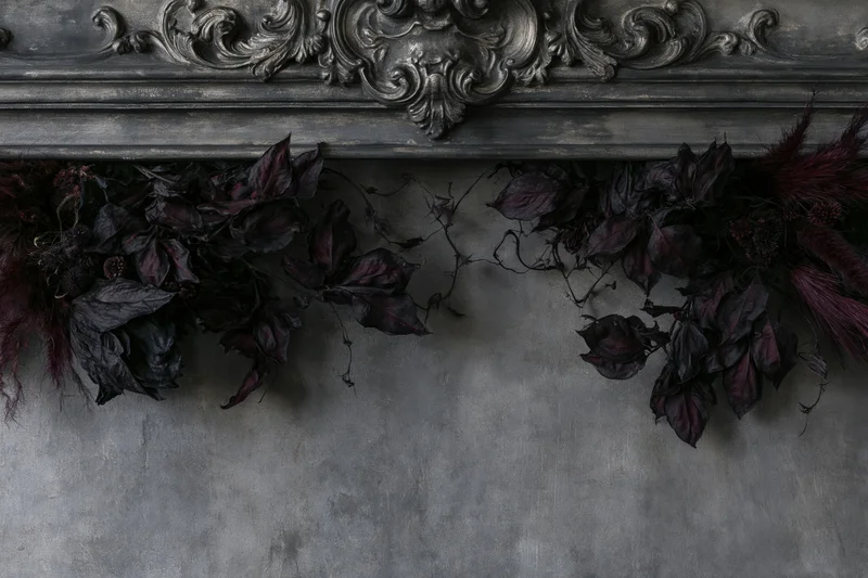 Ornate baroque plaster wall panel with dark dried botanical arrangement above textured gray surface