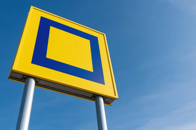 Yellow and blue square logo sign on metal poles against clear blue sky