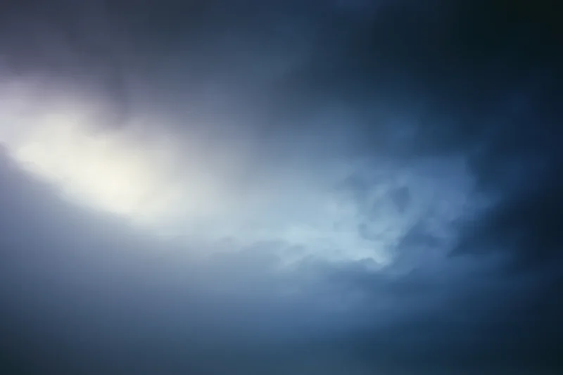 Dark overcast sky at dusk with heavy clouds and soft light breaking through