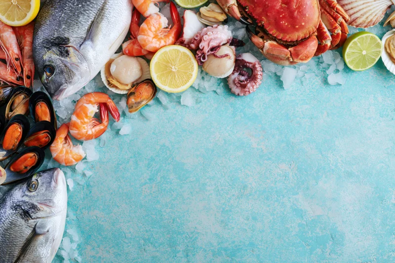Fresh seafood arranged on ice with citrus slices along left edge on blue surface