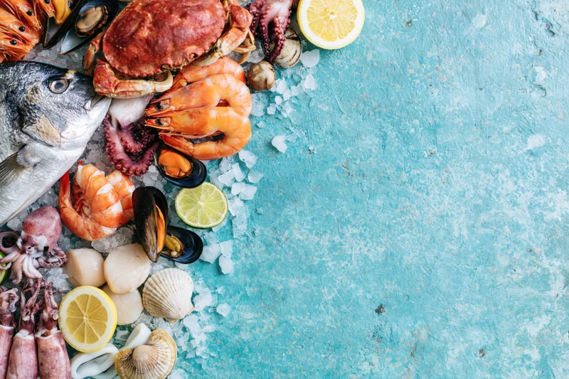 Fresh seafood arranged on ice along left side of blue textured surface