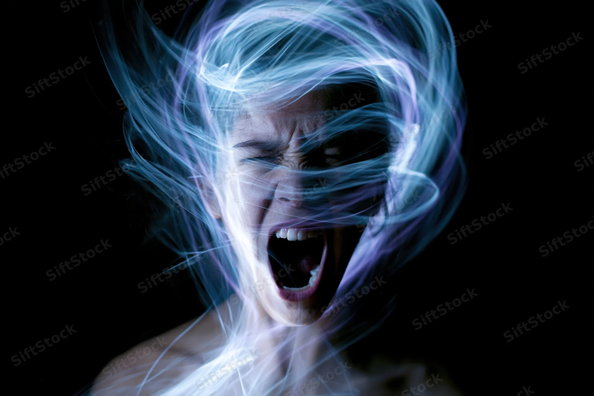 Woman screaming with light trails swirling around her face in a dark studio setting
