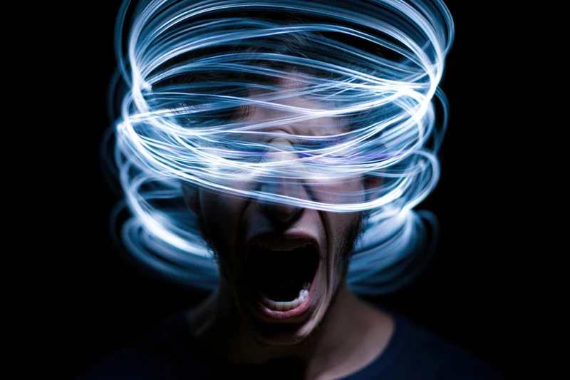 Man screaming with swirling blue light around his head against dark background