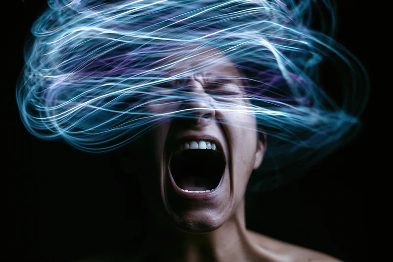 Woman screaming with swirling light trails around her face against dark background