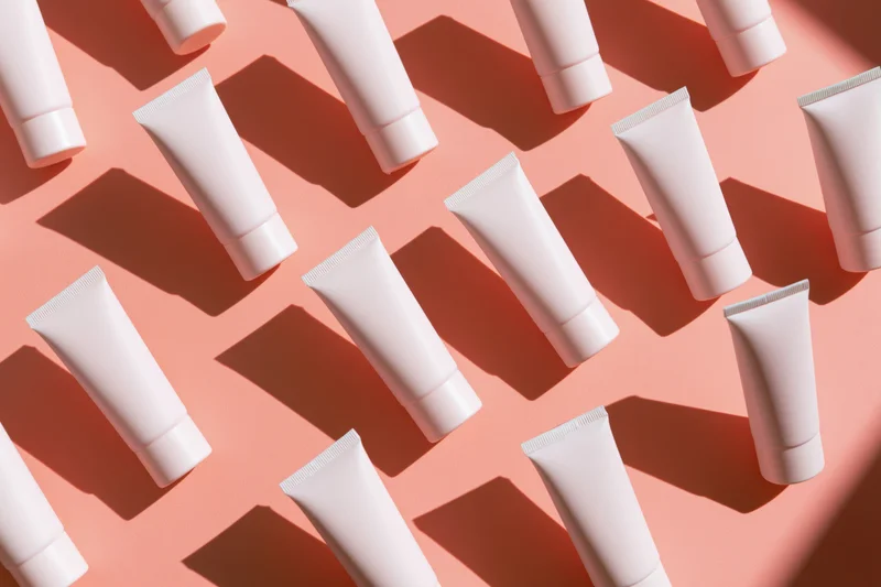 Blank white cosmetic cream tubes arranged in repeating pattern on pink background