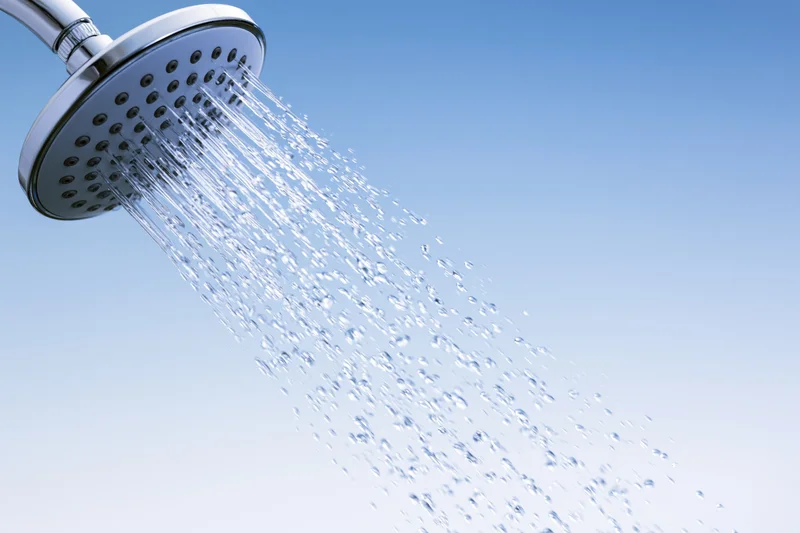 Chrome showerhead spraying water droplets against a blue gradient background