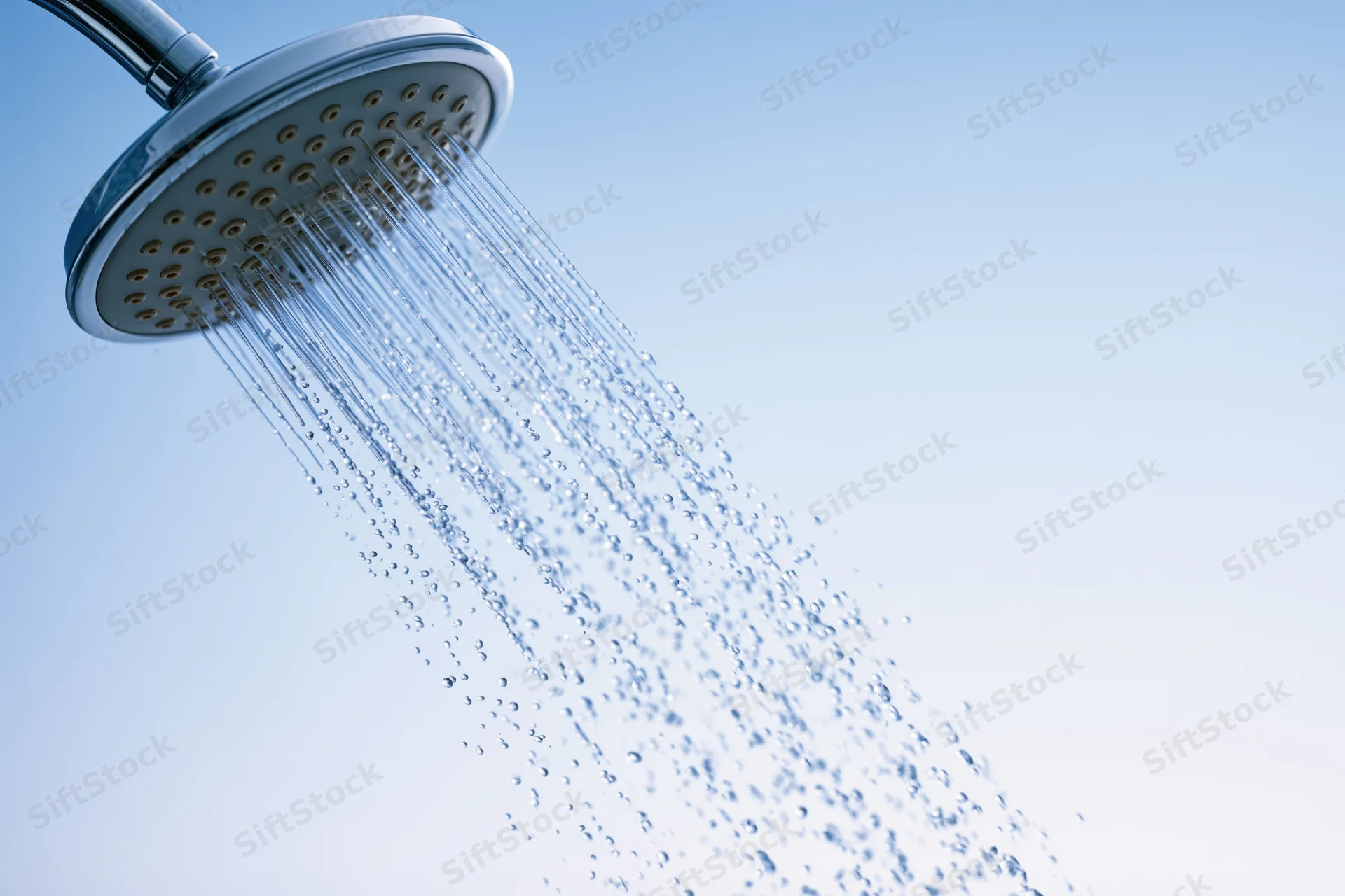 Chrome showerhead spraying water against a light blue background with copyspace on the right