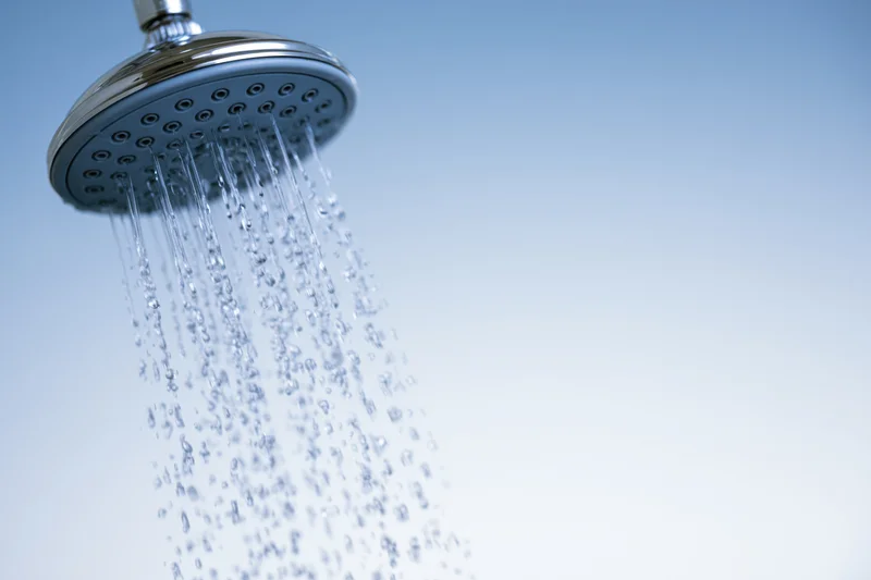 Chrome showerhead spraying water droplets against a light blue gradient background