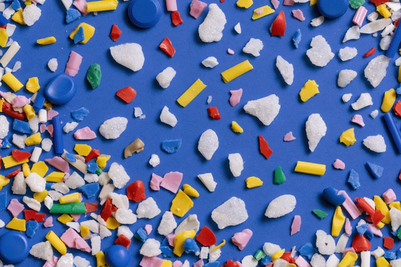 Scattered colorful plastic fragments and microplastic debris on blue background