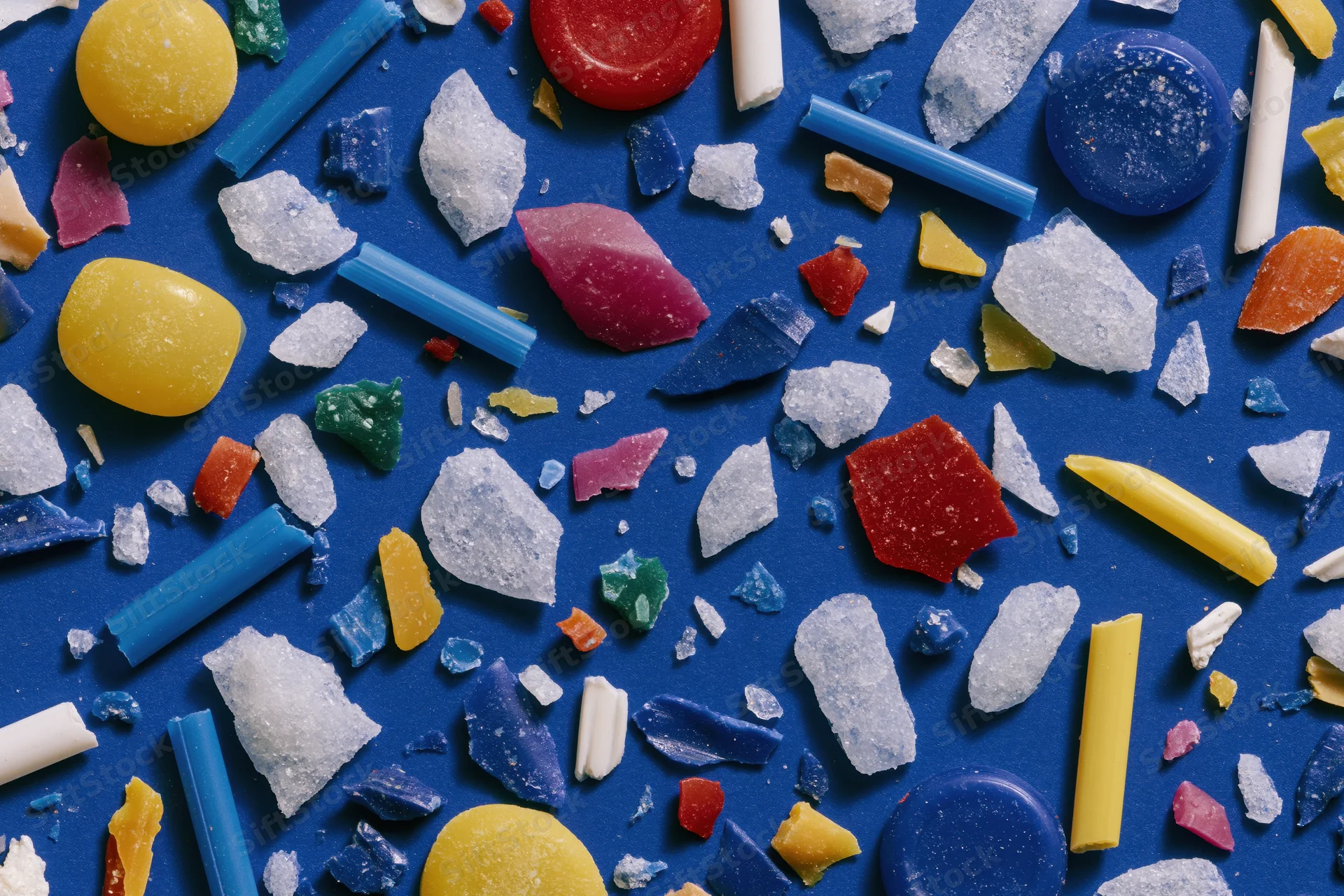 Scattered colorful plastic fragments and microplastics on blue background