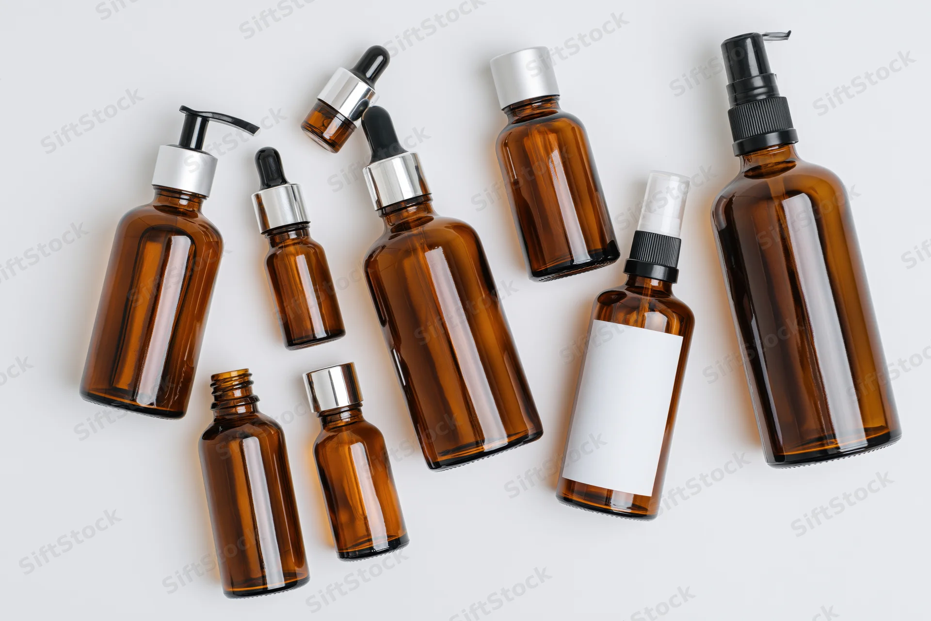 Amber glass bottles with various caps and dispensers arranged in a flat lay on white background