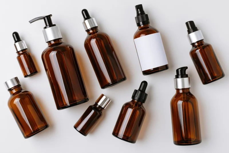 Amber glass bottles with droppers and pumps arranged in a flat lay on white background
