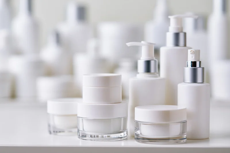 White unlabeled skincare jars and pump bottles arranged on a shelf in a studio setting