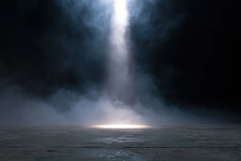 Single spotlight beam cutting down onto a dark concrete floor through smoke