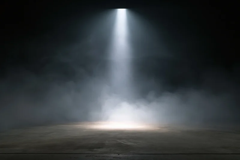 Single spotlight beam shining down on an empty stage floor in a dark smoky theater