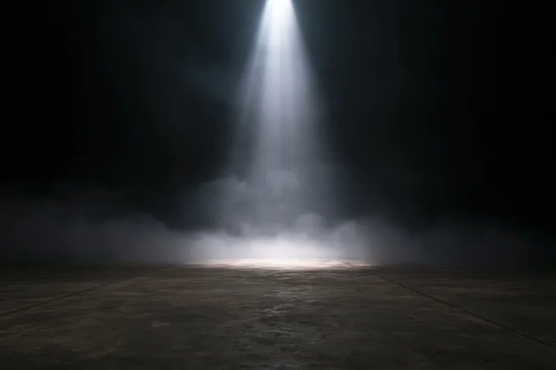 Single spotlight beam illuminating a smoky concrete floor in a dark theater space