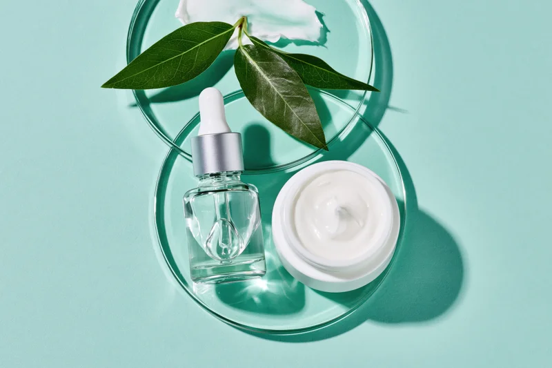 Skincare products arranged with green leaves on a teal background