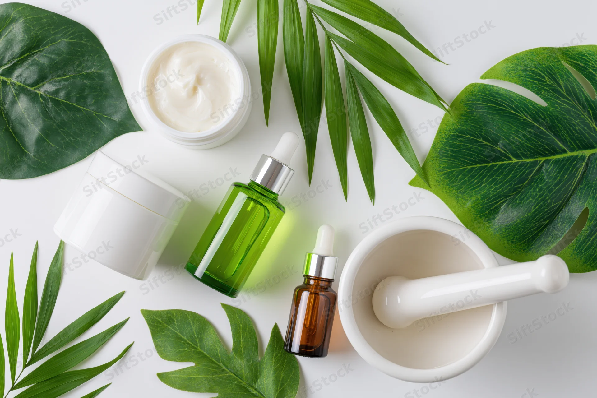 Skincare products and green leaves arranged on white surface in flat lay composition