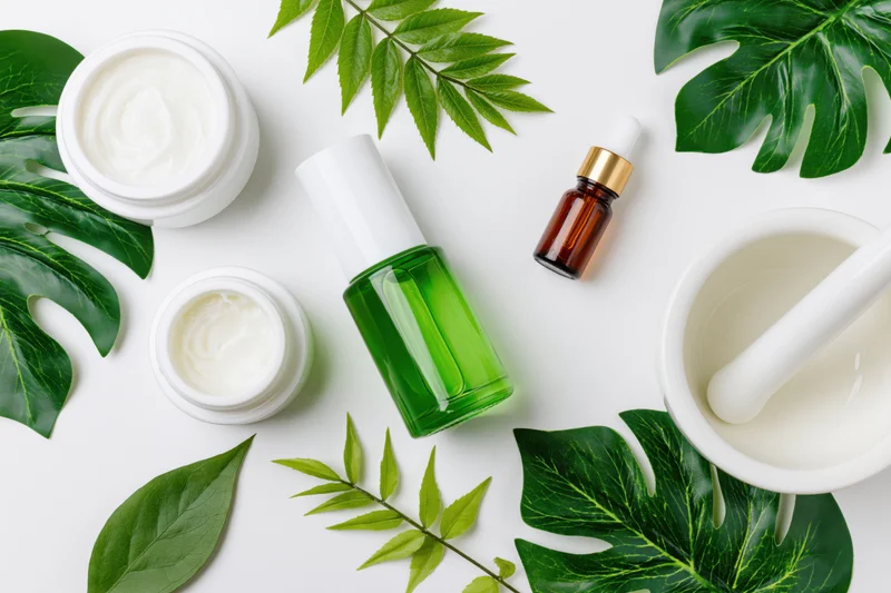 Skincare products and green leaves arranged on white surface in flat lay composition