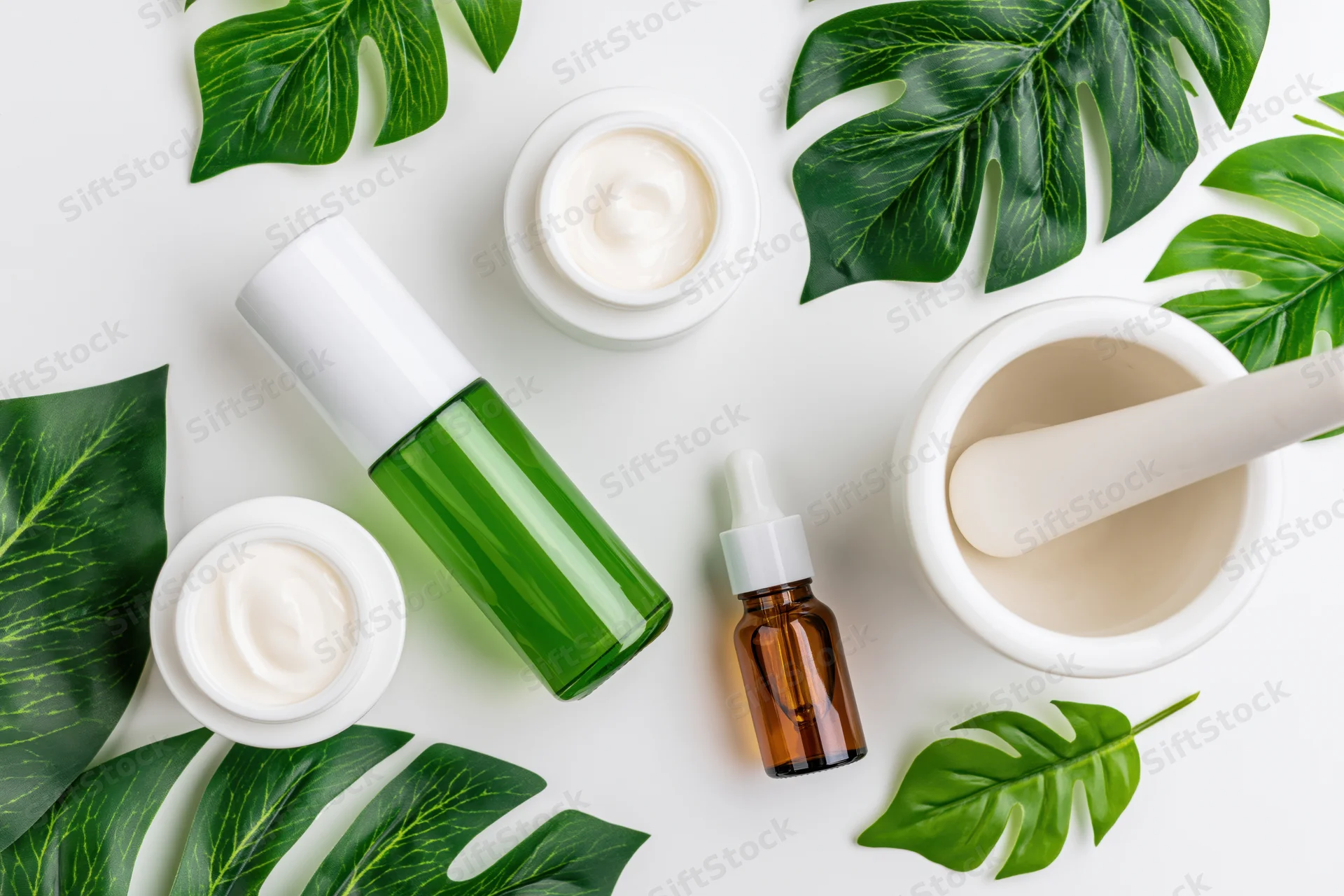Skincare products and monstera leaves arranged in flat lay on white surface