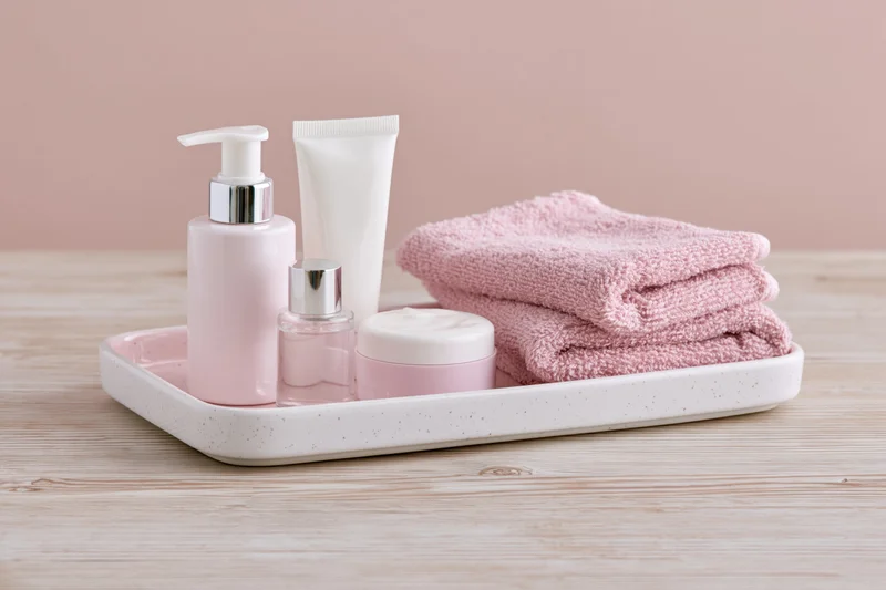 Skincare products arranged on a white ceramic tray with a pink towel on a wooden surface