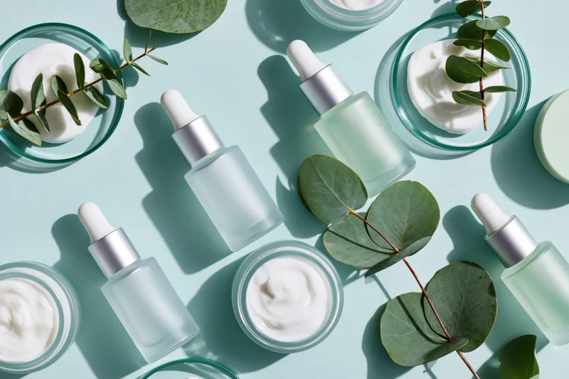 Skincare products and eucalyptus leaves arranged in flat lay on mint blue surface