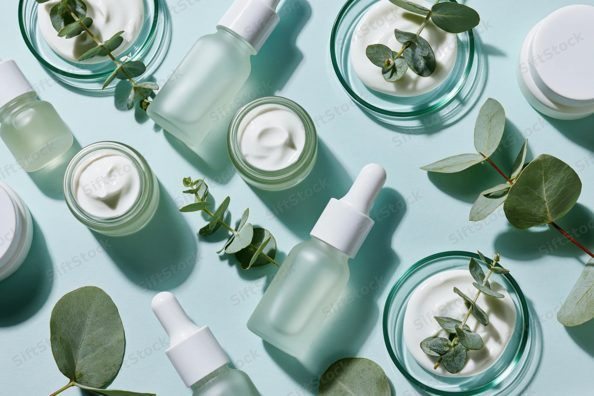 Skincare products and eucalyptus leaves arranged in flat lay on mint blue surface