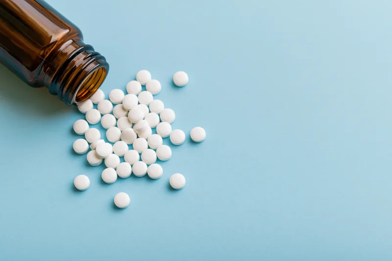 White pills spilled from an amber glass bottle on a blue surface