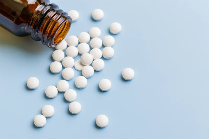 White pills spilled from an amber glass bottle on a blue surface