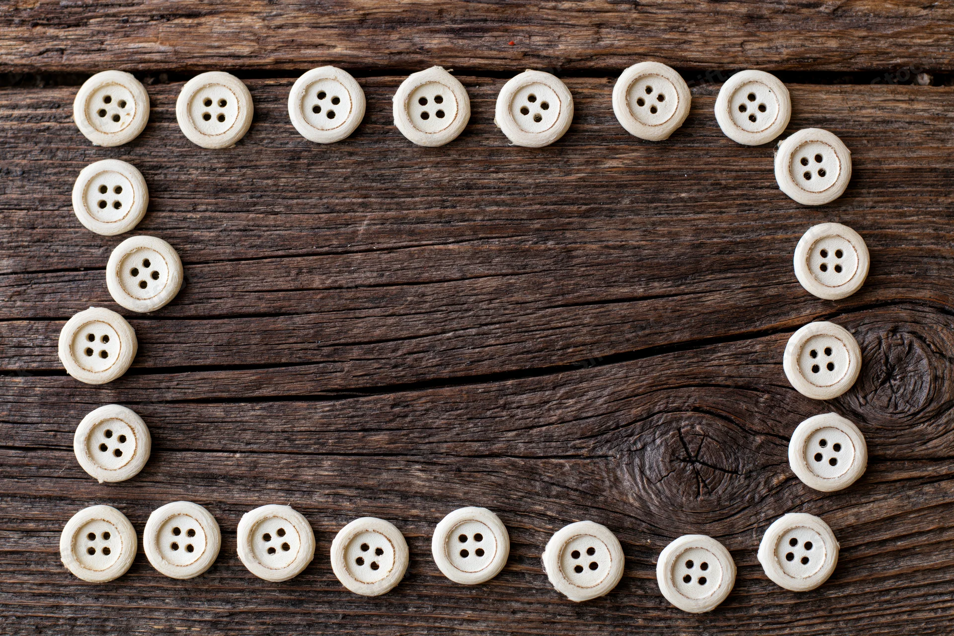 Cream-colored sewing buttons arranged in a circular frame on a rustic wooden surface