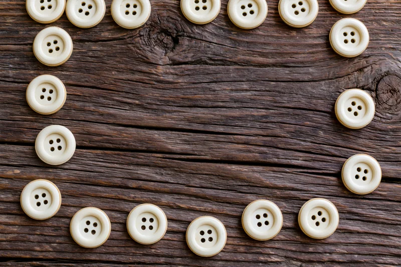 Cream buttons arranged in a frame on a rustic wooden surface with copyspace in center